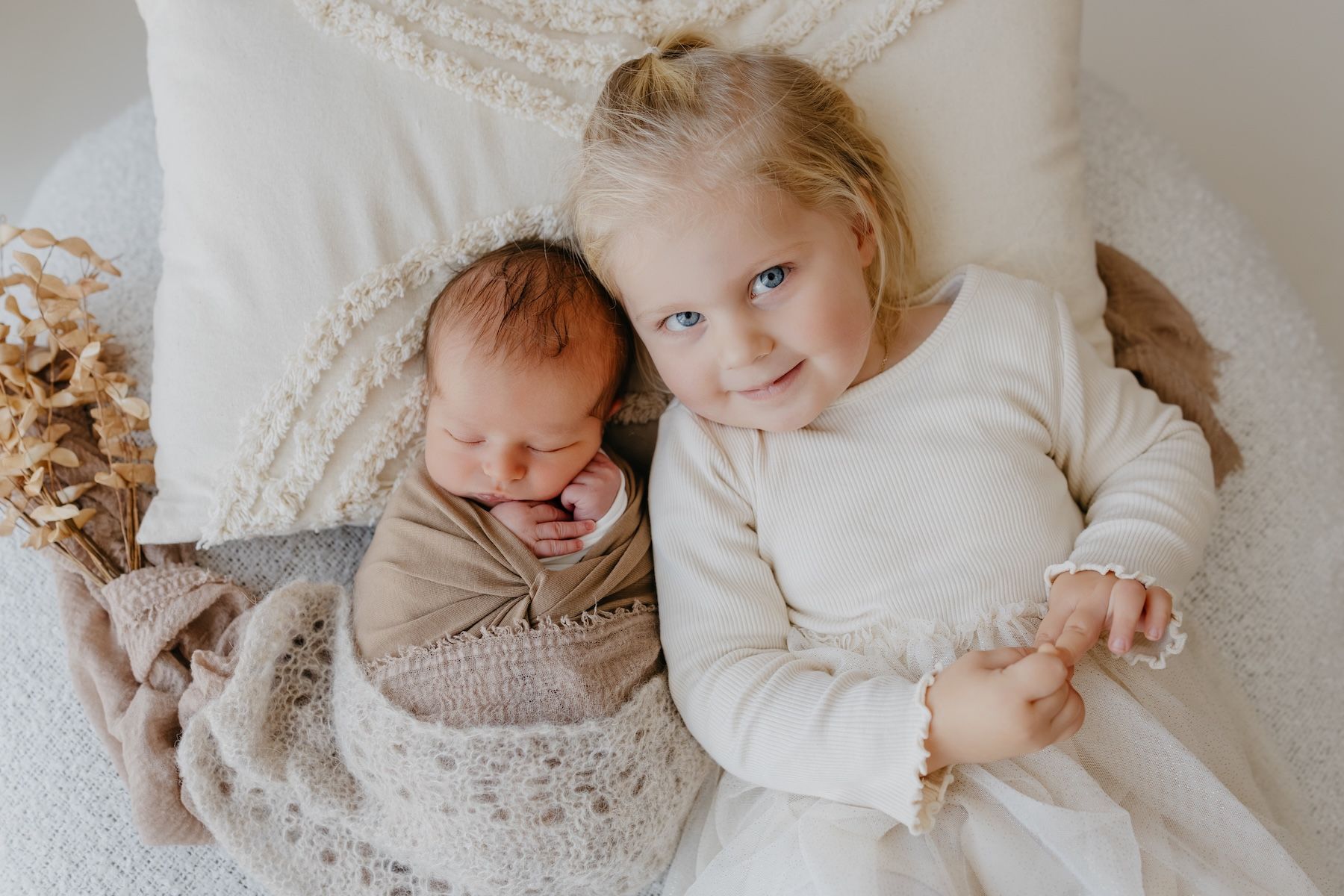 Zärtliches Newborn-Geschwisterfoto, in dem das ältere Kind das Baby liebevoll hält und eine ruhige, geborgene Atmosphäre entsteht